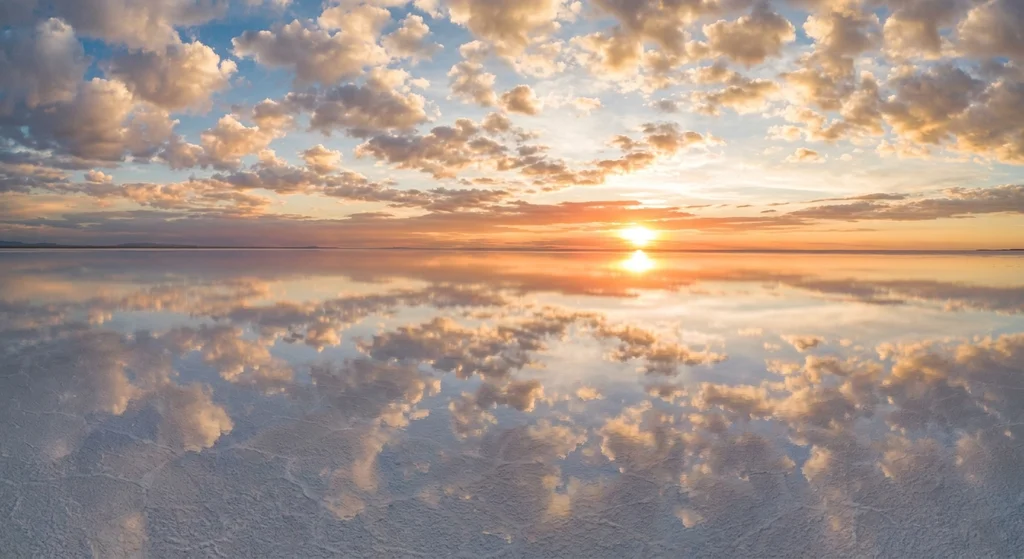 Natural Phenomena That Look Like CGI - A vast salt flat covered in a thin layer of water perfectly reflecting a cloudy blue sky and sunset.